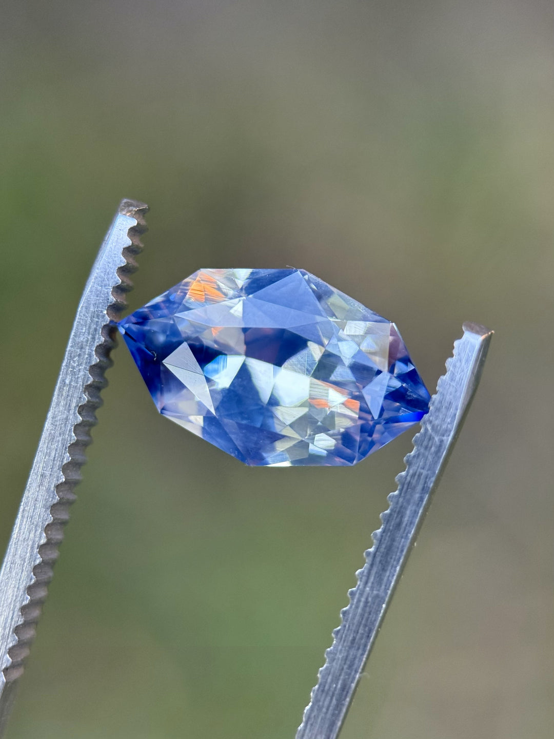 Macro photo of 5.00CT blue white parti sapphire held in gemstone tweezers, highlighting the crisp facets, mixed marquise shape, and brilliant blue and white reflections of the unheated gemstone from Madagascar.