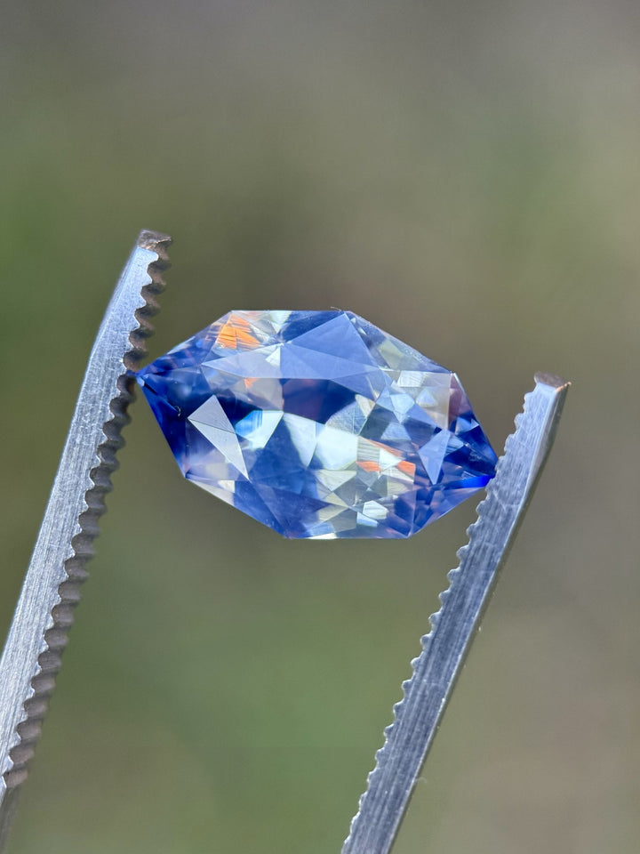Macro photo of 5.00CT blue white parti sapphire held in gemstone tweezers, highlighting the crisp facets, mixed marquise shape, and brilliant blue and white reflections of the unheated gemstone from Madagascar.