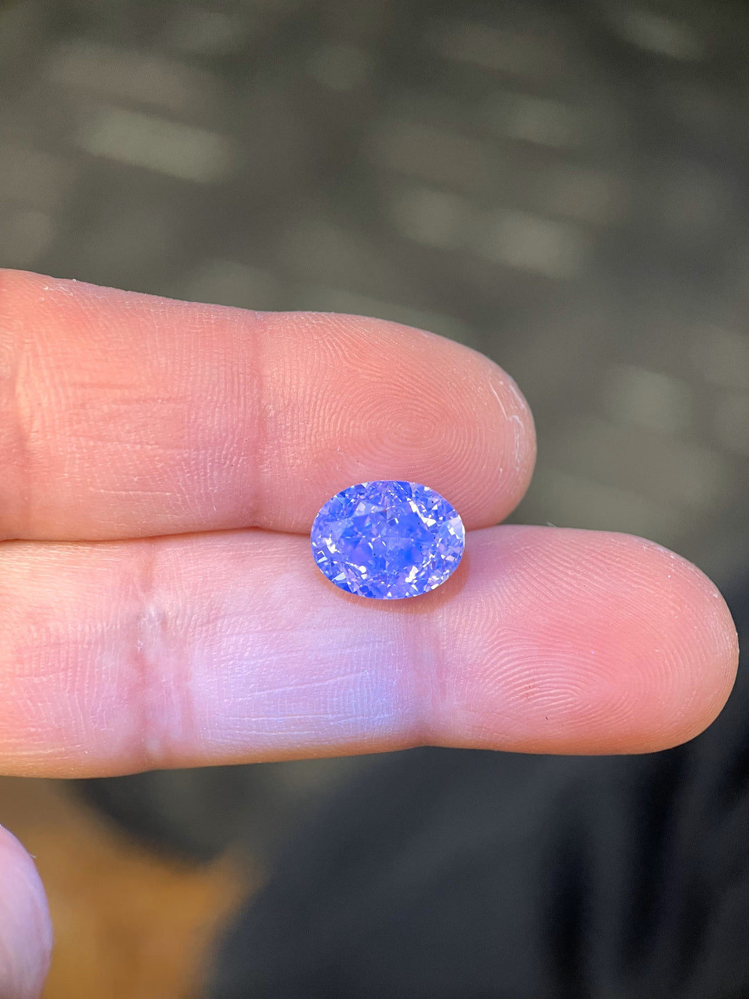 5.25ct Oval Brilliant Diamond held between fingers, glowing with a striking blue fluorescence under UV light, showcasing its unique optical properties.