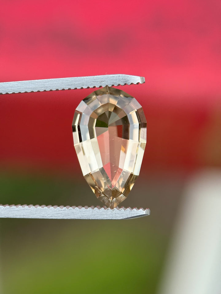 Champagne brown tourmaline gemstone weighing 5.36 carats held in gemstone tweezers, showcasing geometric pear step cut facets and golden-brown reflections, ethically mined natural gem from Congo, Africa