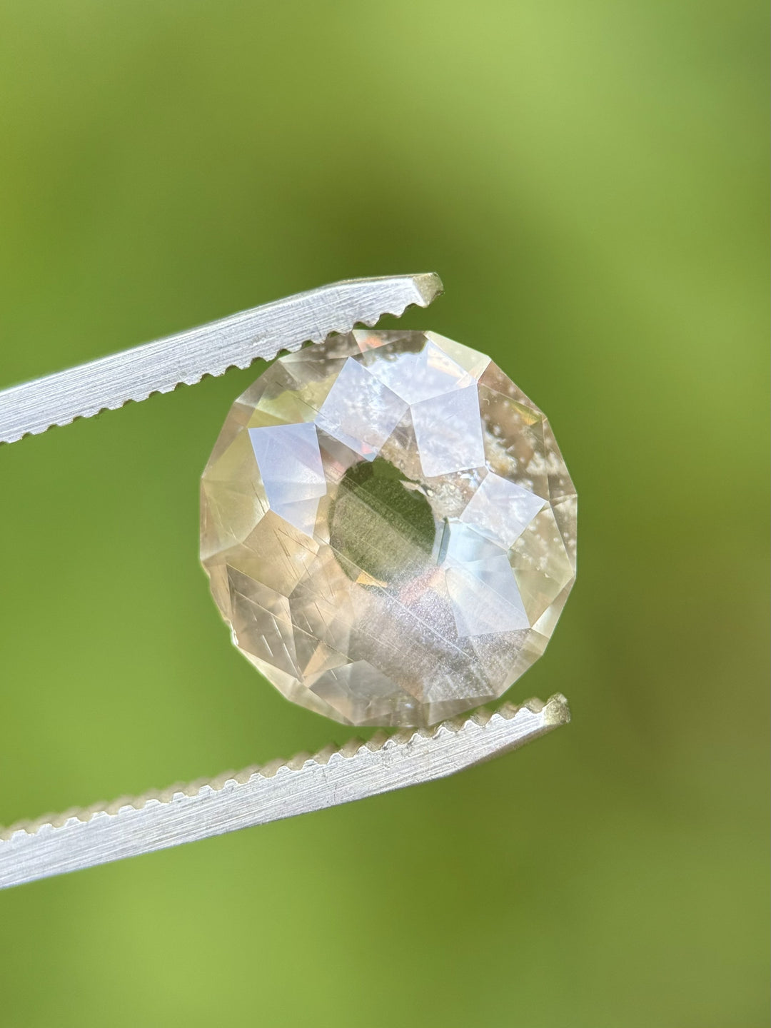 Close-up of 6.38 carat sapphire from Umba River, Tanzania, held in gem tweezers showing precision Portuguese-style faceting with earthy color palette