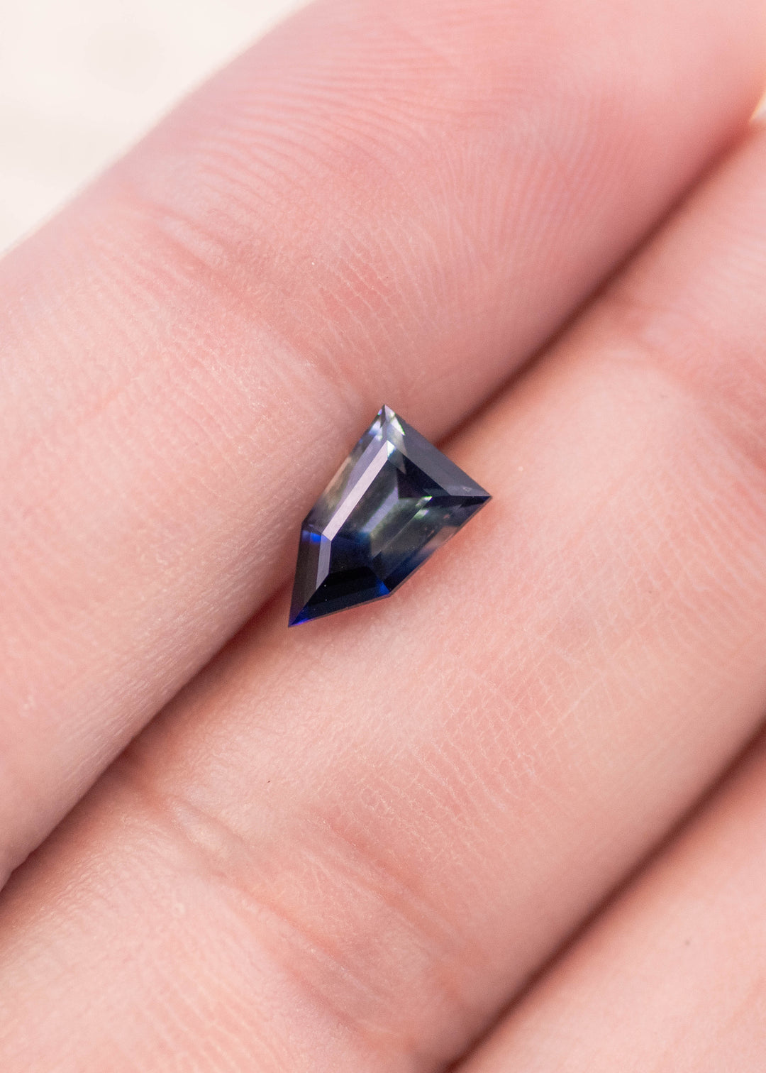 1.22 carat bi-color parti sapphire resting on fingertips, featuring colorless to blue tones in a pentagon shield step cut, natural untreated sapphire from Ratnapura Sri Lanka