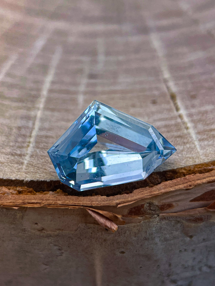 A 2.23-carat blue sapphire in a free-form geometric cut resting on a wooden surface, showing its deep blue tones and clean craftsmanship. Origin: Sri Lanka, Untreated.