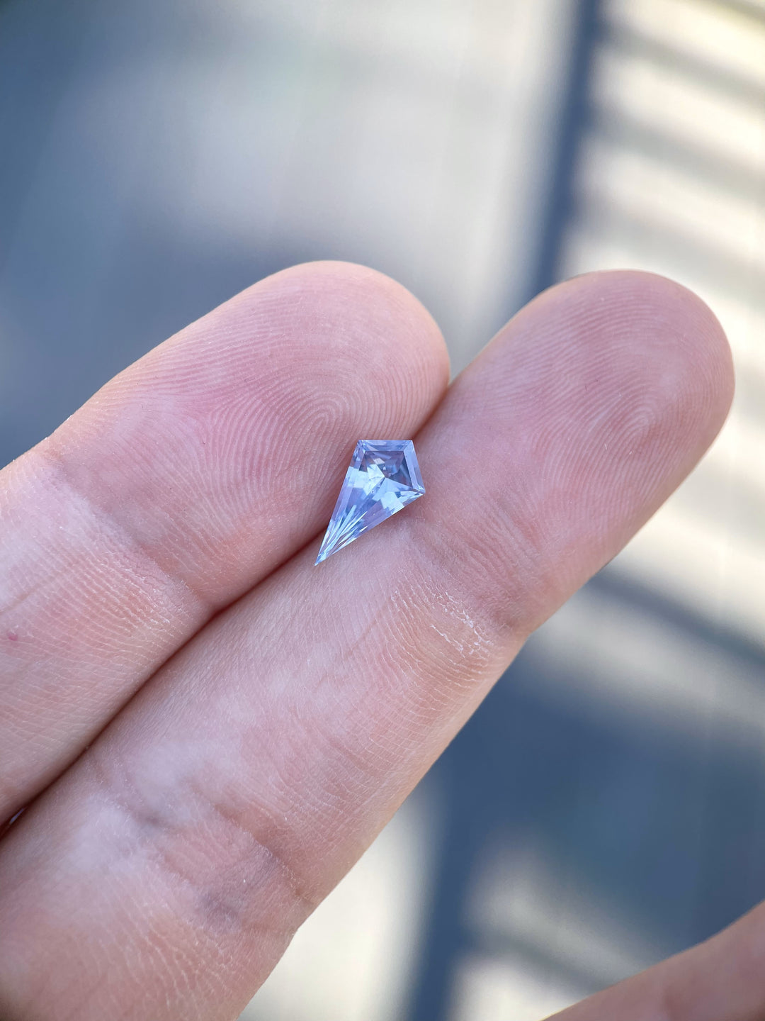 Artful composition featuring a 1.66 carat geometric step cut kite sapphire, highlighting its powder blue and periwinkle hues, against a serene, natural background.
