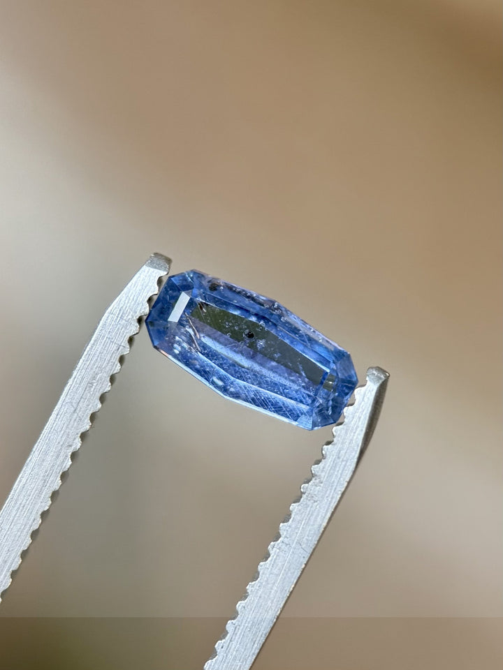 Close-up of 1.05ct natural cornflower blue sapphire from Tanzania held in gem tweezers – showcasing custom elongated cushion step cut