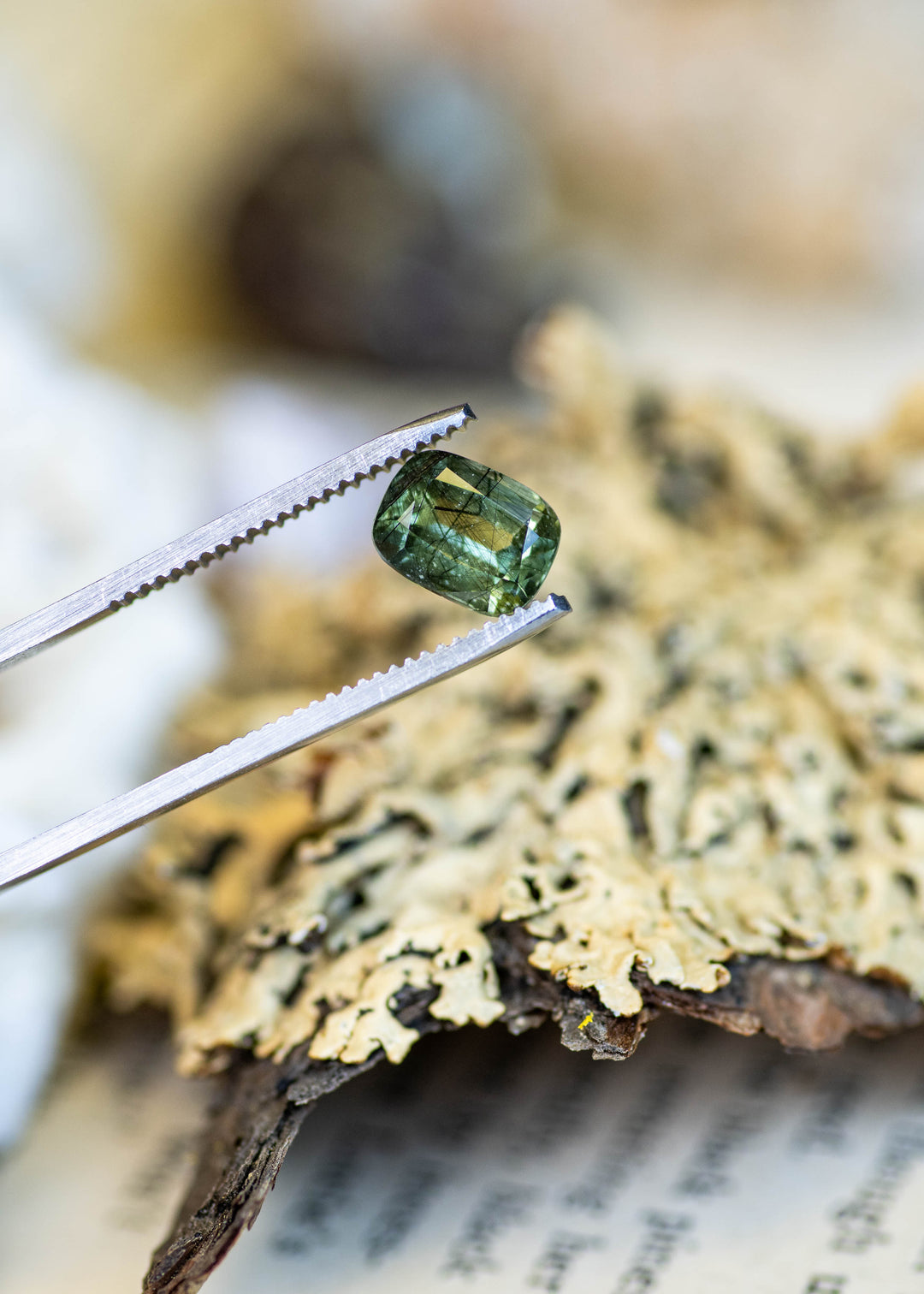 Close-up of a natural 2.72 carat ombre soft green peridot from Pakistan held in tweezers, highlighting its cushion mix cut and natural internal crystal structure.