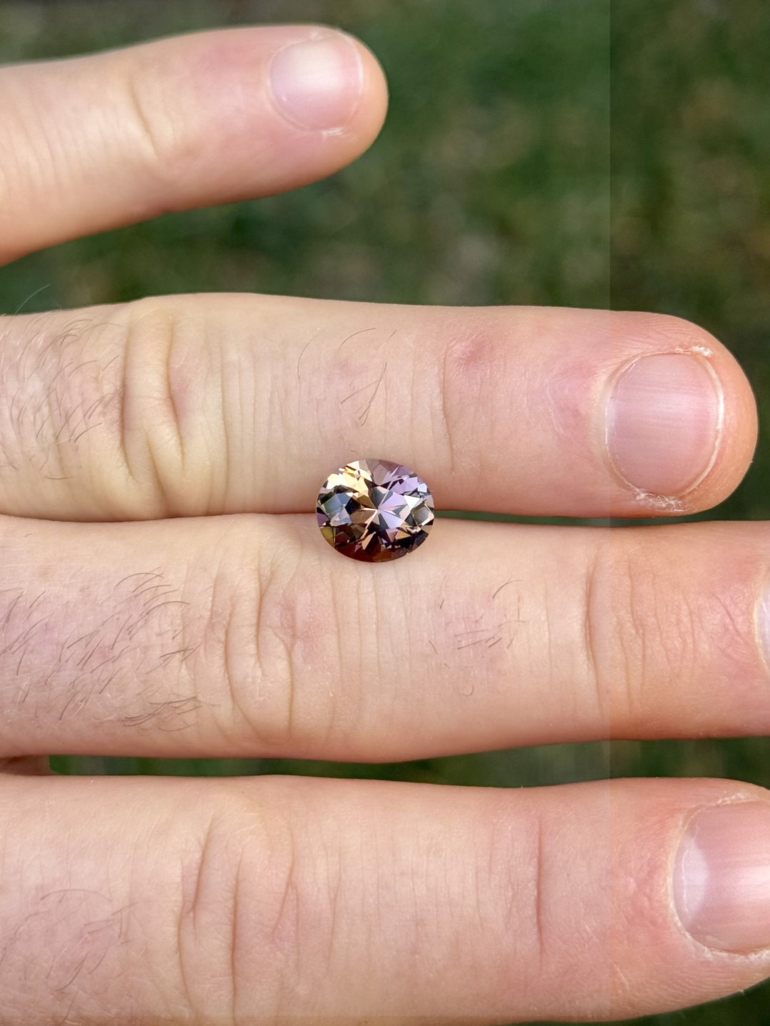 2.76ct Tanzanite on fingertips for scale, revealing custom roval cut and fancy color range from orangish peach to pink and purple, unheated