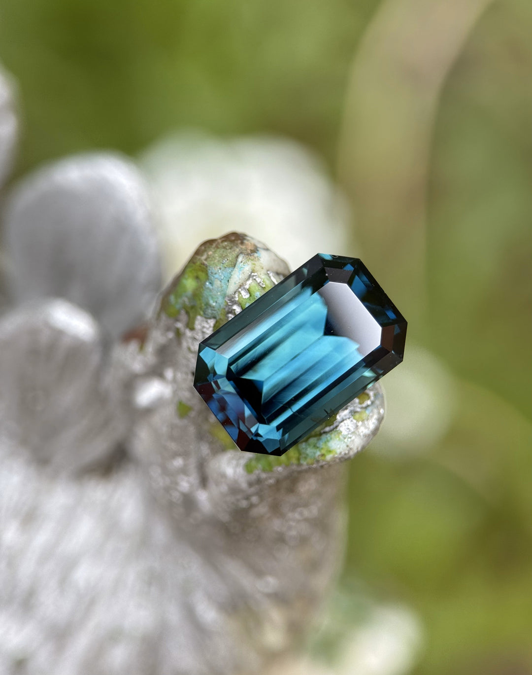 Close-up of a 5.85 carat peacock sapphire placed on a sculpture, showcasing its rich teal and blue tones with precise emerald step cut.