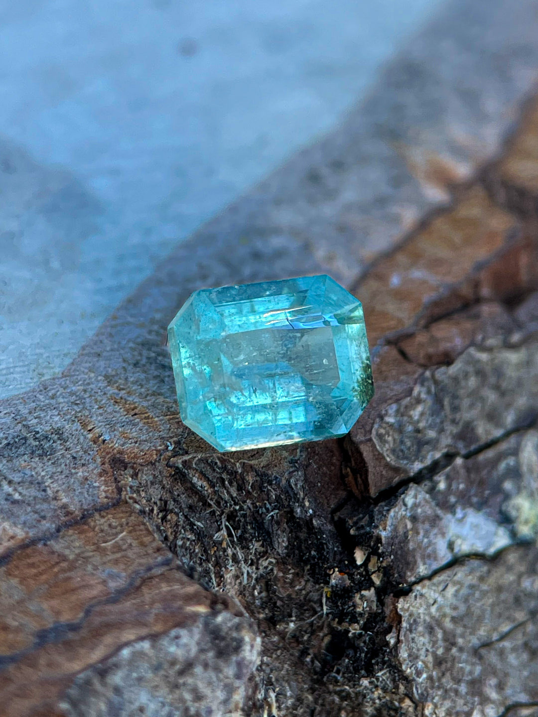 1.17-carat green-blue emerald cut gemstone displayed on a natural rock surface.
