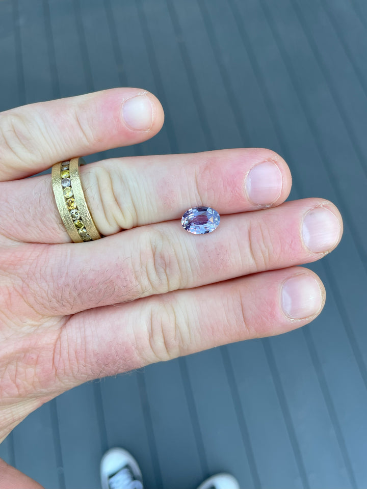 A mix brilliant oval-cut purple sapphire from Sri Lanka, weighing 2.56 carats, displayed against natural surroundings, untreated and vibrant.