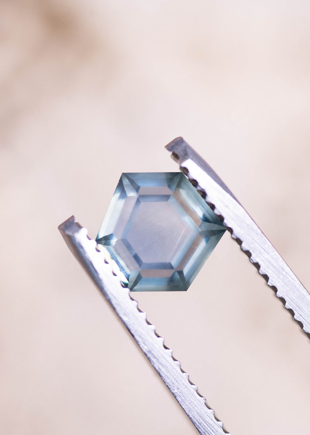Geometric hexagonal step cut teal blue seafoam sapphire held in gem tweezers, highlighting the precision cut facets, light performance, and untreated Montana sapphire clarity at 1.37 carats.