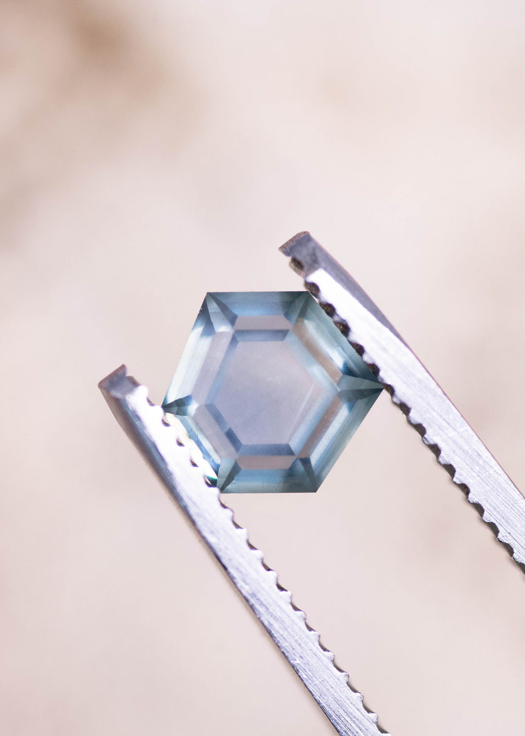 Geometric hexagonal step cut teal blue seafoam sapphire held in gem tweezers, highlighting the precision cut facets, light performance, and untreated Montana sapphire clarity at 1.37 carats.