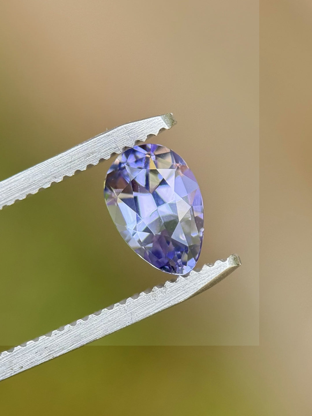 Close-up of 1.40ct Tanzanite in tweezers showing lilac, blue, and purple flashes – precision peared oval cut, no heat treatment