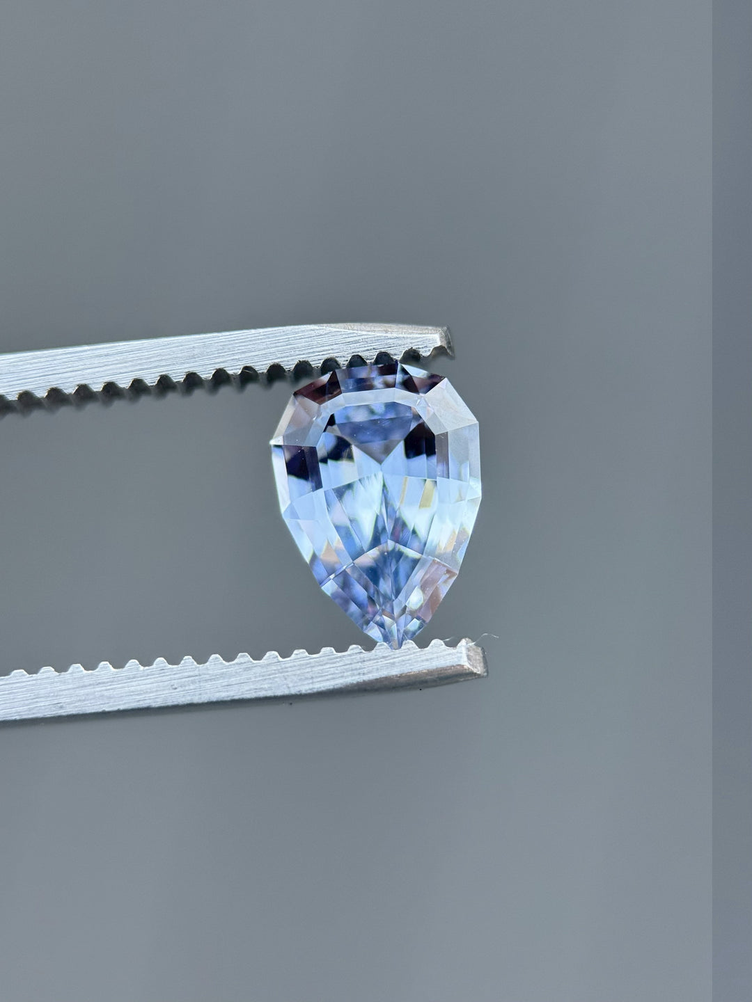 Macro shot of an unheated 1.67-carat blue sapphire held in tweezers, showcasing precision geometric pear brilliant faceting