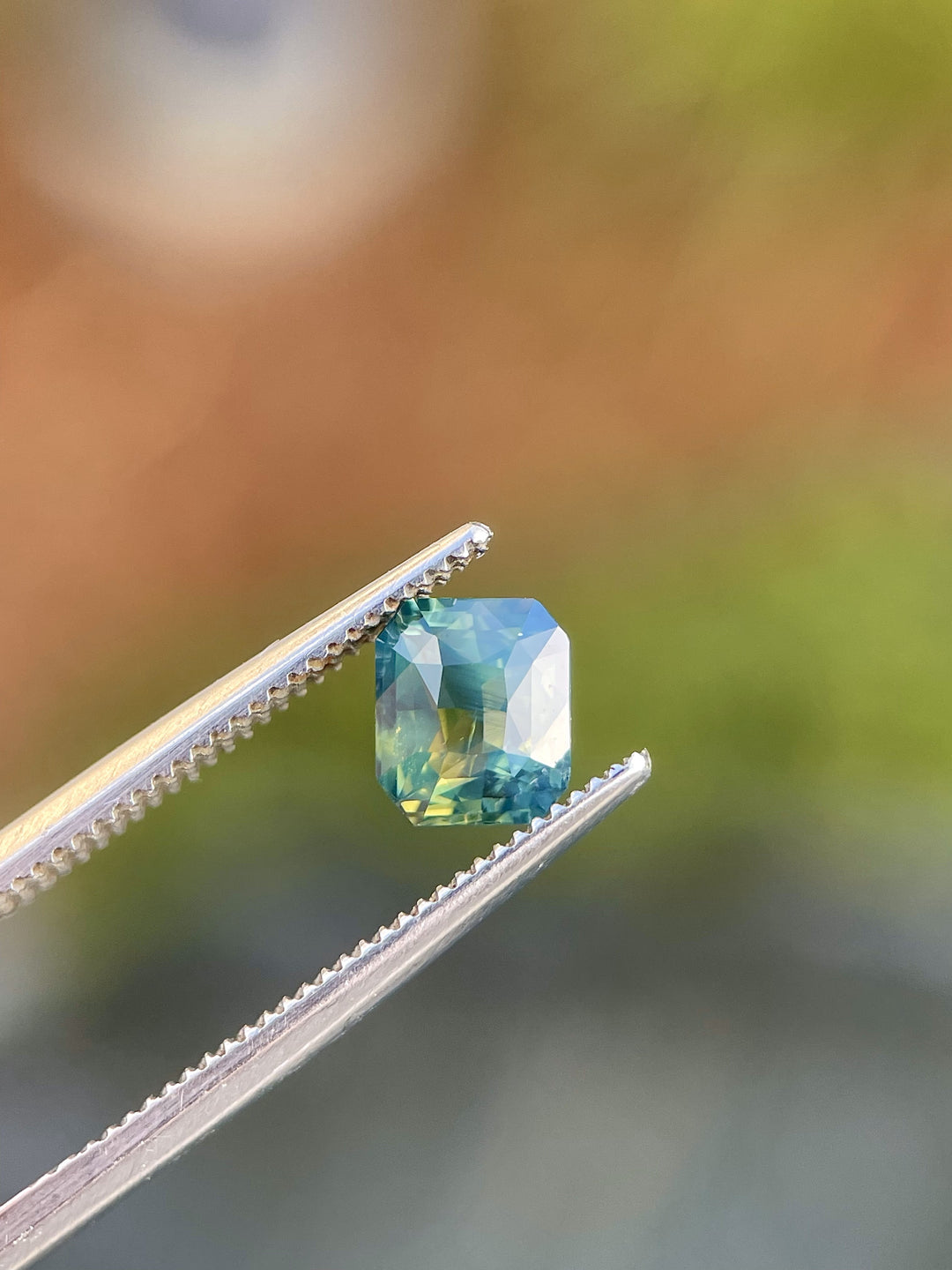 A radiant-cut sapphire weighing 1.42 carats. The gemstone highlights a stunning play of yellow, teal, and green hues, untreated and sourced from Madagascar.