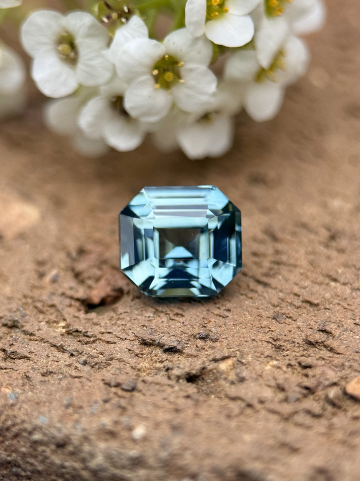 Close-up of a 2.14-carat emerald cut sapphire in vivid sky blue, placed on a fingertip for scale and visual brilliance.