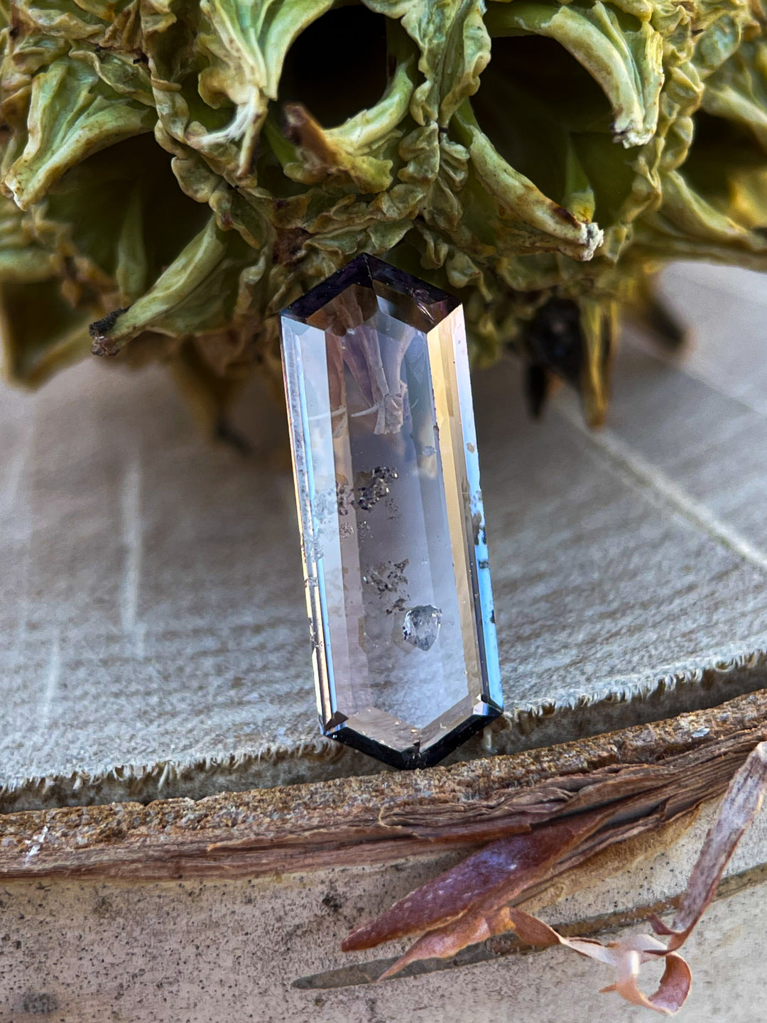 A natural spinel gemstone placed against a textured background, featuring a hexagonal portrait cut with a mix of purple and pink tones.