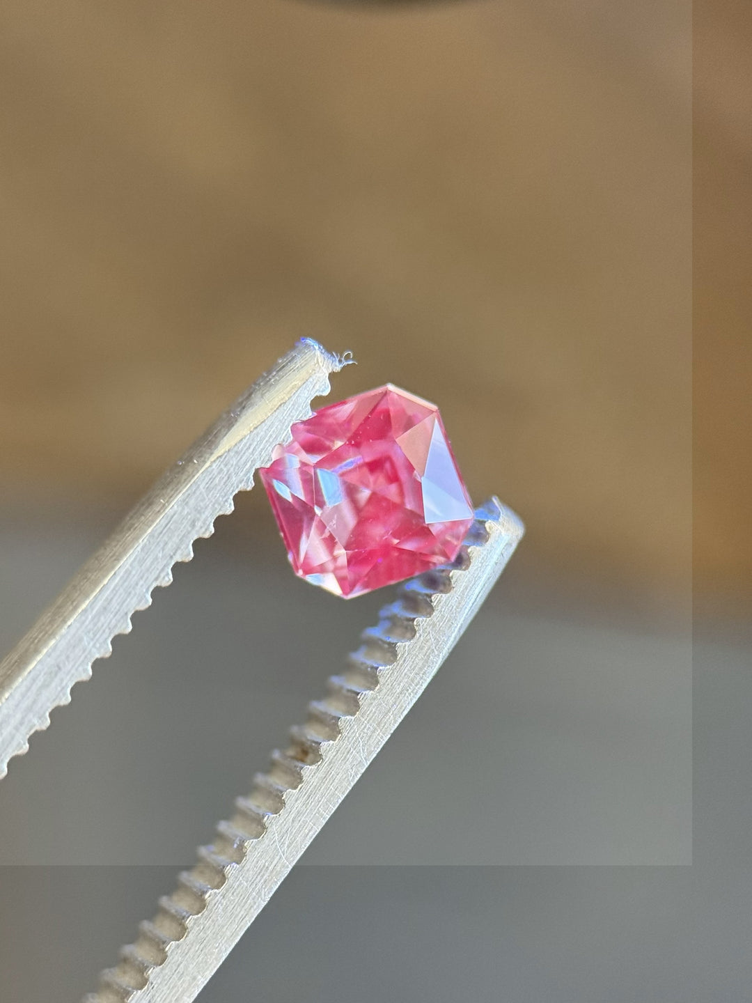 Vivid pink gemstone in radiant cut held in tweezers – unrelated stone shown for color contrast or comparison