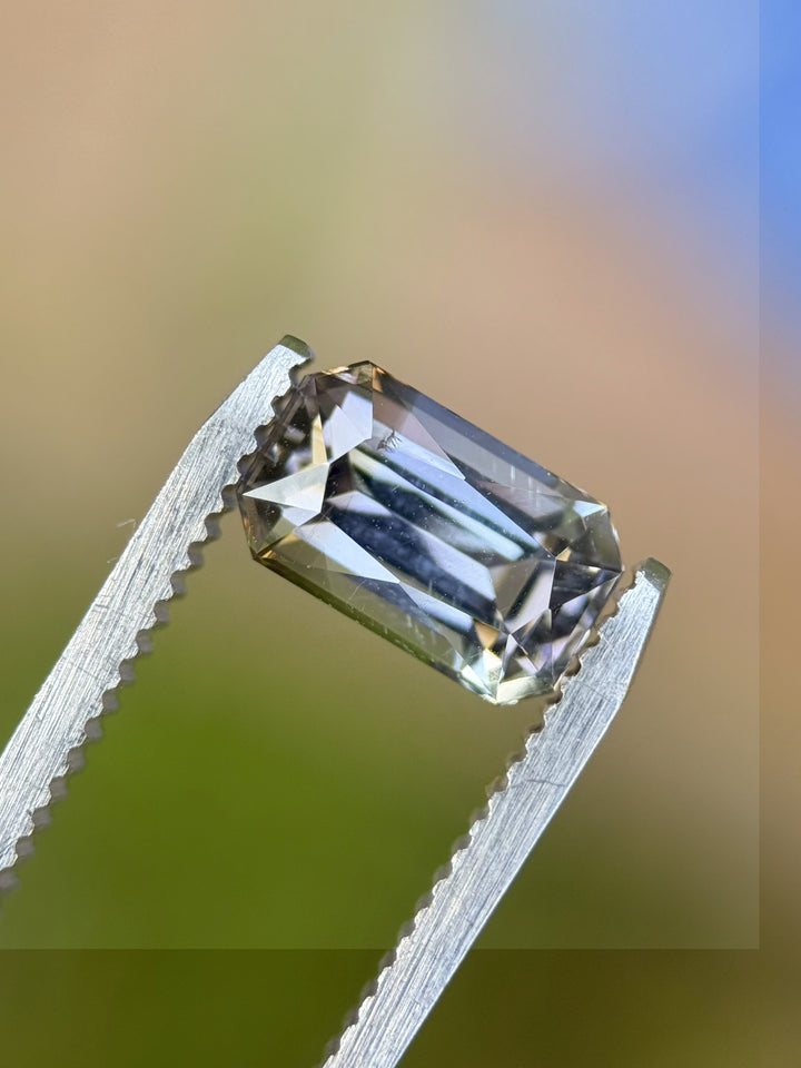 2.32 carat radiant-cut tanzanite held in gem tweezers, showcasing color blend of grey, teal, green, and purple – ethically sourced