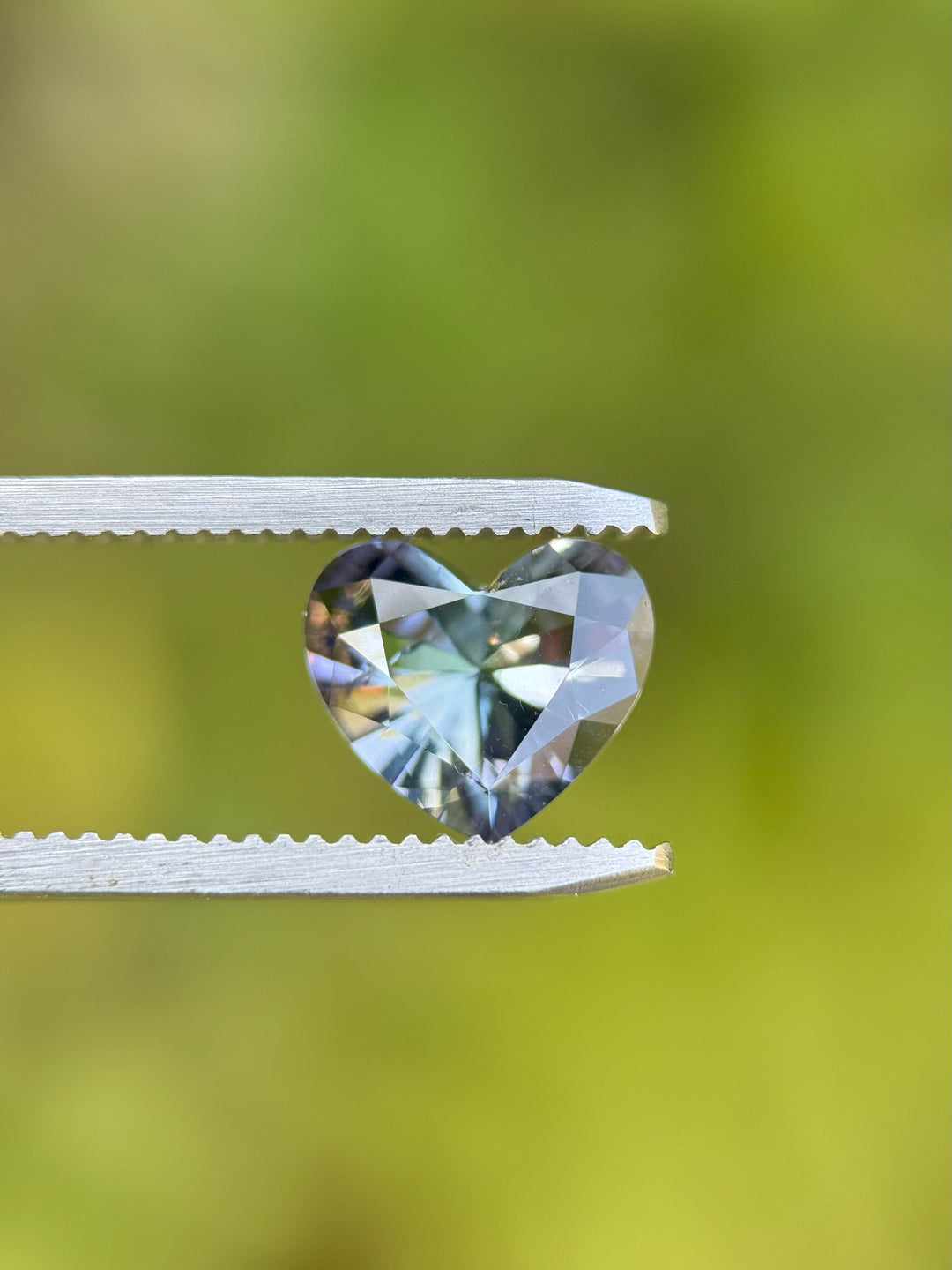 Close-up of custom brilliant heart-cut Tanzanite with vivid teal, lavender, and blue colors held in tweezers