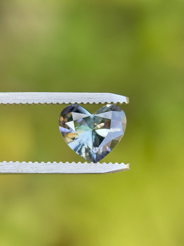 Close-up of custom brilliant heart-cut Tanzanite with vivid teal, lavender, and blue colors held in tweezers