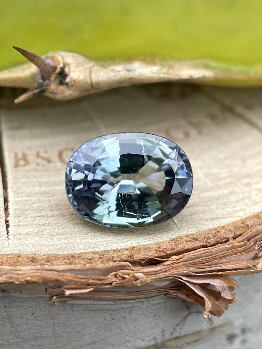 2.02 carat Tanzanite displayed on a wood surface, revealing its unheated mermaid coloration with teal, green, and purple reflections.