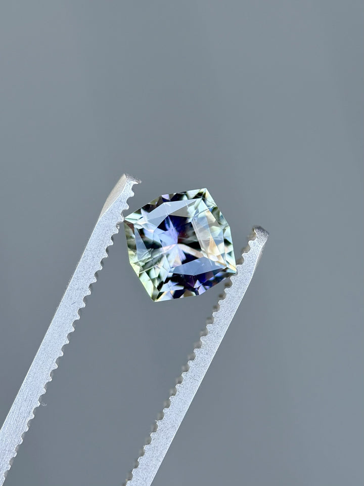 Top view of 1.55 carat Tanzanite with vivid teal, purple, and green hues in ultra-precision kite cut held by gemstone tweezers