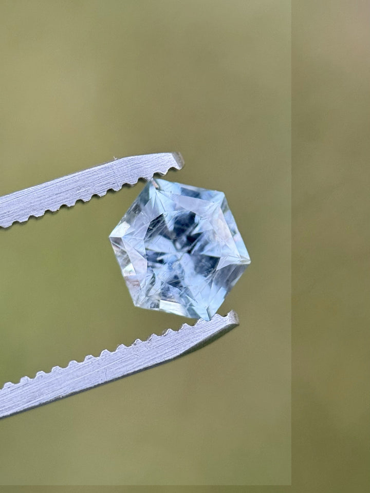 Teal blue Montana sapphire held in tweezers showing custom hexagonal brilliance