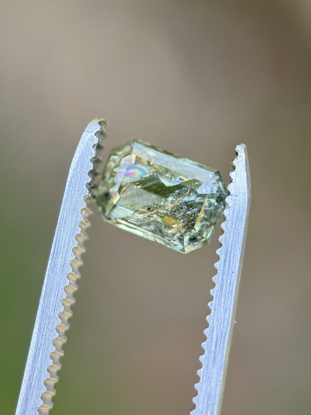 Close-up of a 2.06 carat Tanzanian sapphire held in tweezers, unheated with earthy yellow-green brilliance
