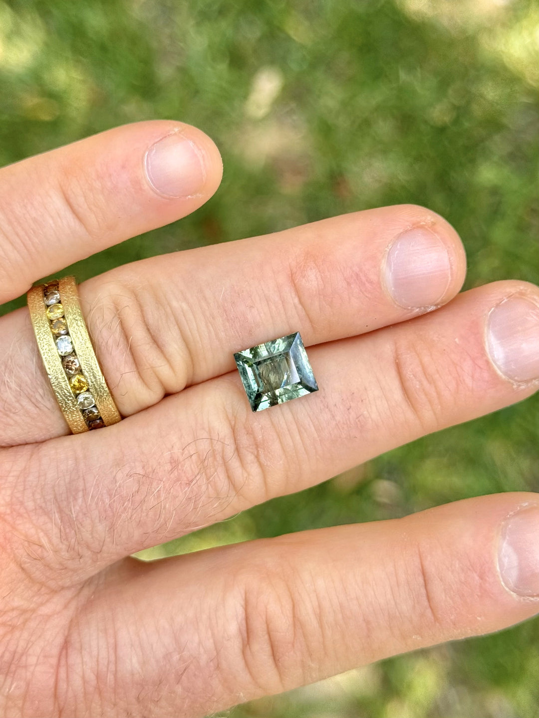 (Finger outdoor): Large antique-style carre cut sapphire with teal green tones displayed on hand
