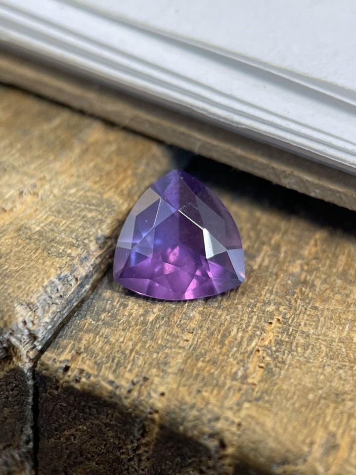 Artistic display of a 0.94ct untreated pink and purple sapphire in a custom trillion cut, resting on a weathered wood surface.