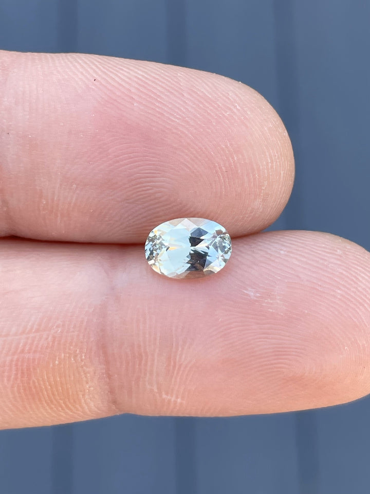 A close-up of a 2.05-carat oval-cut sapphire with gray and yellow hues, delicately held in tweezers to highlight its brilliance and precision cut.