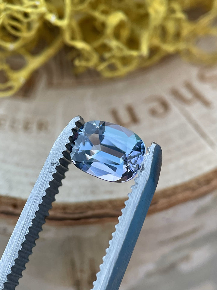 A natural, untreated 1.36ct Tanzanite gemstone with a modified cushion cut, showcasing vibrant teal and blue colors against a neutral background.