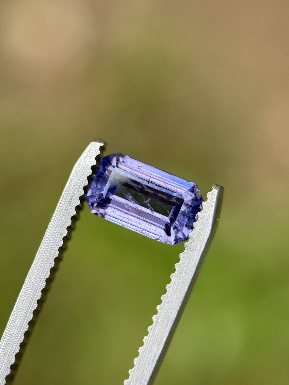 Close-up of 1.74ct violet sapphire held in tweezers, highlighting open culet and precision emerald cut