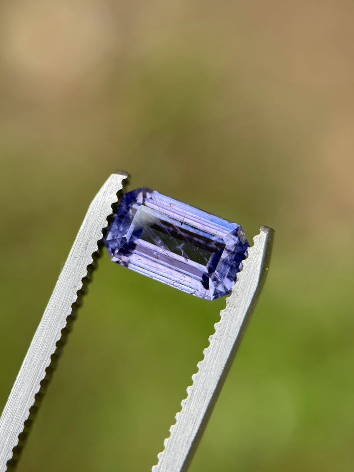 Close-up of 1.74ct violet sapphire held in tweezers, highlighting open culet and precision emerald cut