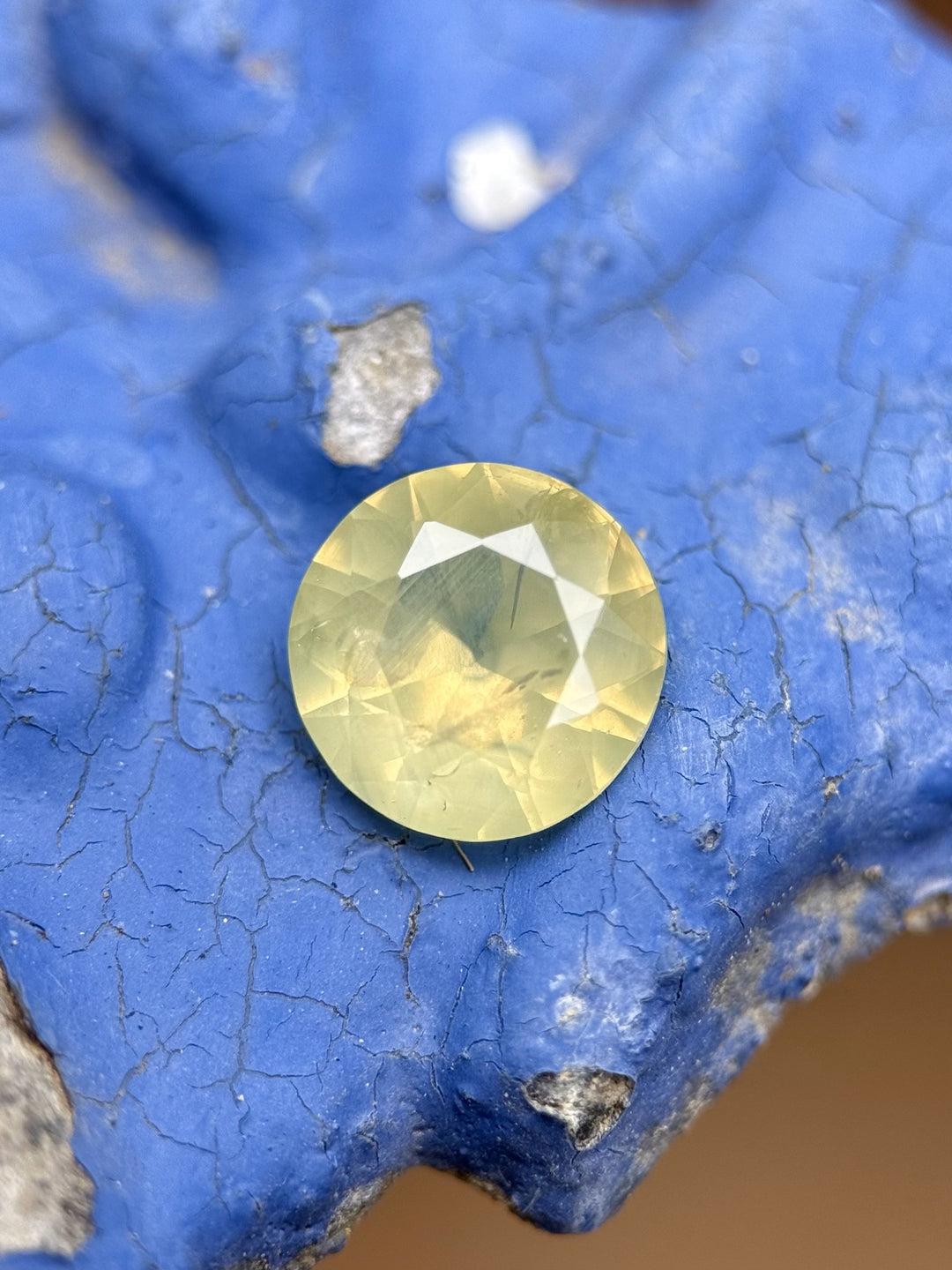 Close-up of untreated round brilliant 2.32ct sapphire on blue surface, showing lemon lime and opalescent tones