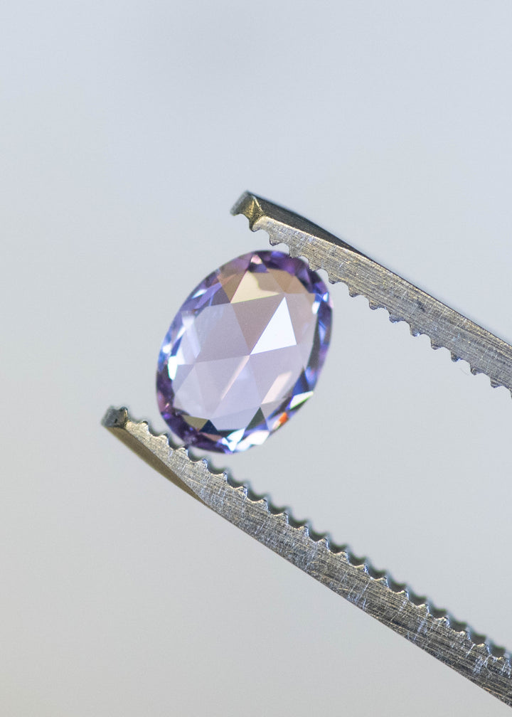 Natural unheated violet pink sapphire held in tweezers, highlighting oval mix cut brilliance and pastel purple color saturation.