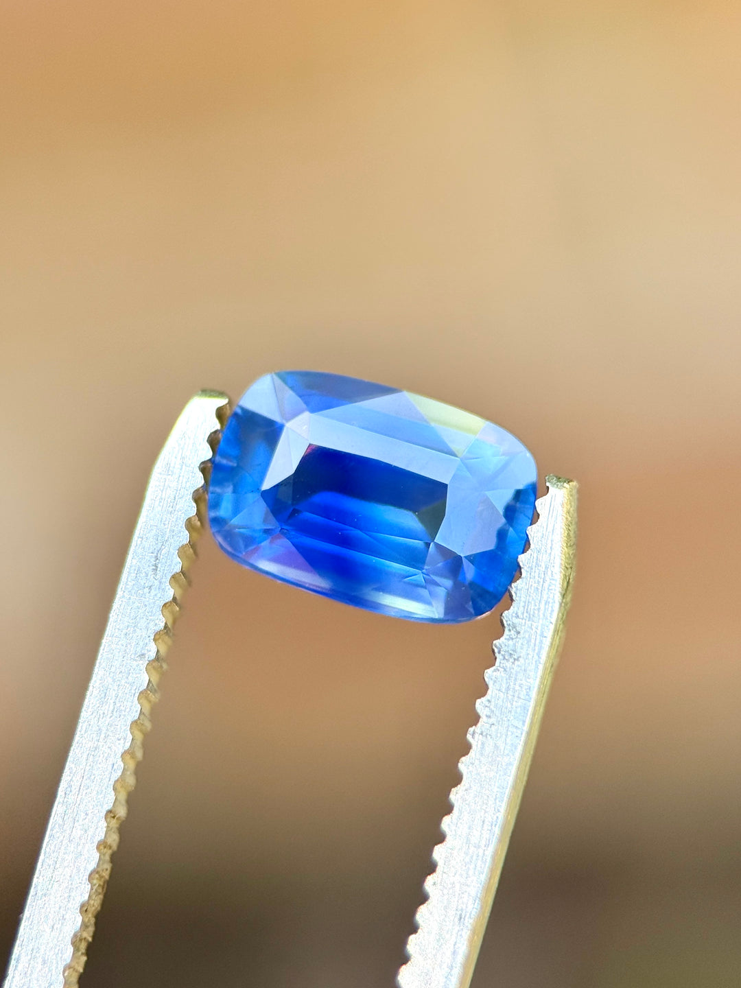 Natural unheated cornflower blue sapphire held in tweezers, highlighting elongated cushion proportions and royal blue flashes across the crown facets.