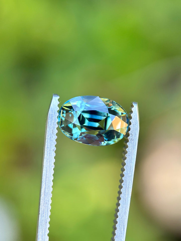 Natural unheated green teal blue parti sapphire held in tweezers, highlighting exceptional color separation and precision-cut brilliance.