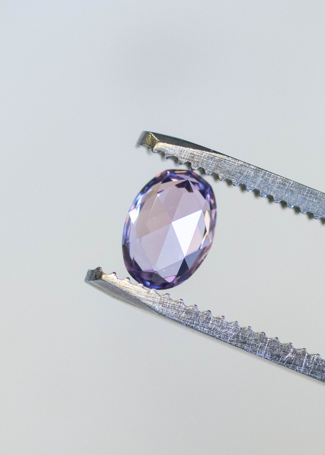 Natural unheated lavender pink sapphire held in tweezers, highlighting rose cut faceting and delicate pink-violet tones.