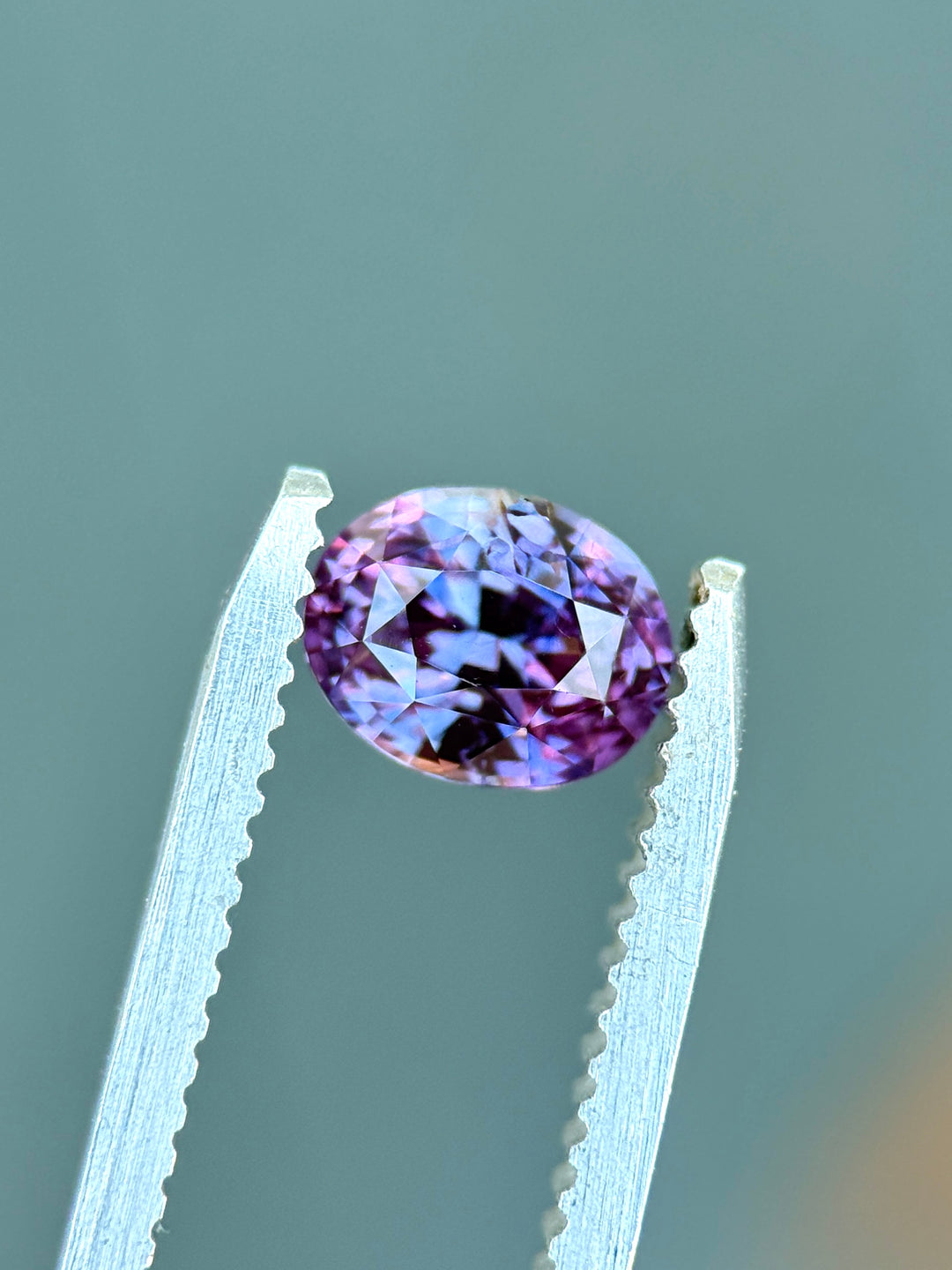 Natural unheated pink purple sapphire held in tweezers, highlighting brilliant oval symmetry and vivid magenta-violet flashes.