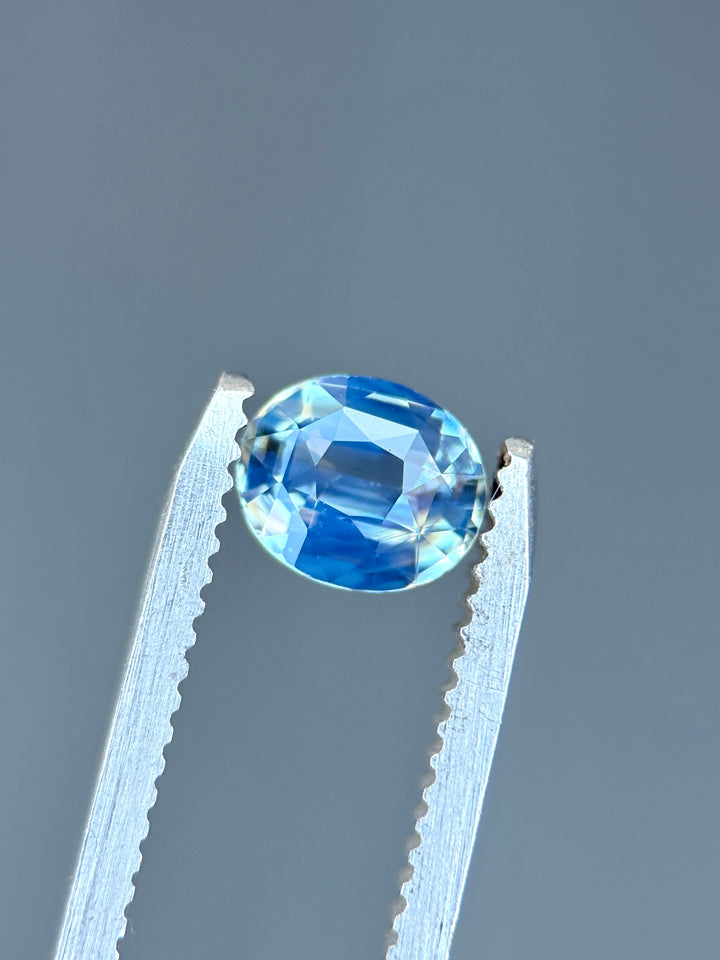 Natural unheated powder blue sapphire held in tweezers, highlighting precision oval proportions and luminous opalescent glow.
