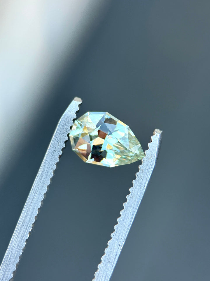 Natural unheated seafoam green sapphire held in tweezers, highlighting elegant pear shape and bright mint-green brilliance.