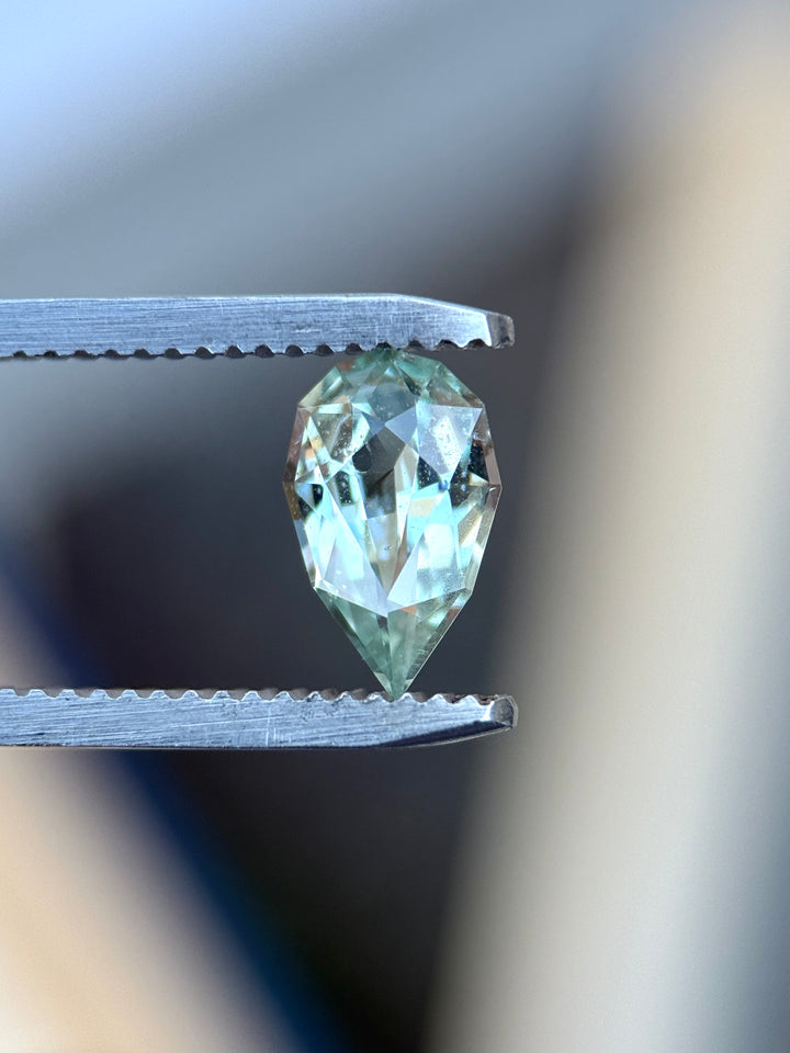 Natural unheated seafoam green sapphire held in tweezers, highlighting elegant pear shape and bright aqua-green brilliance.