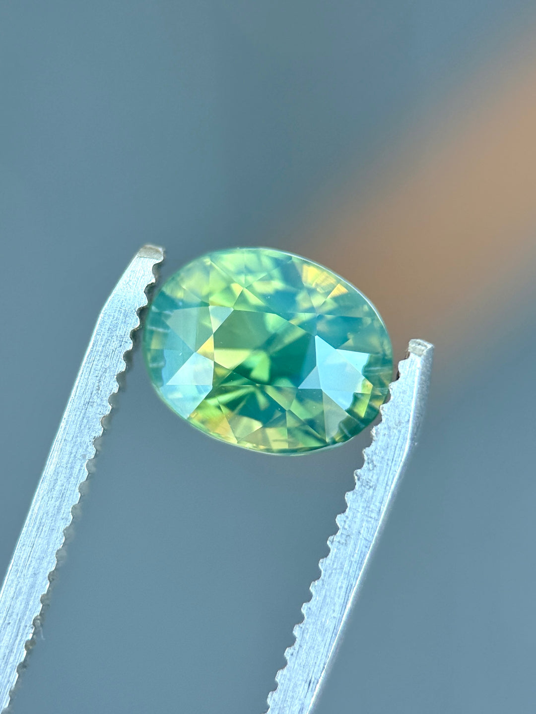 Natural unheated teal blue green parti sapphire held in tweezers, highlighting ocean-toned color transitions and precision-cut brilliance.