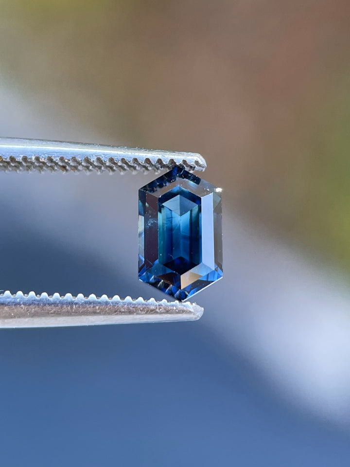 Close-up of a 1.31-carat sapphire from Gombe, Nigeria, held in precision tweezers. This emerald-cut gem radiates blue-green brilliance.