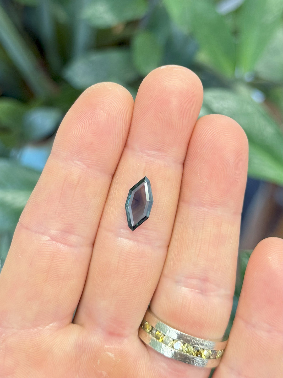 Sapphire resting on fingers to show scale and color transition between teal and inky blue.