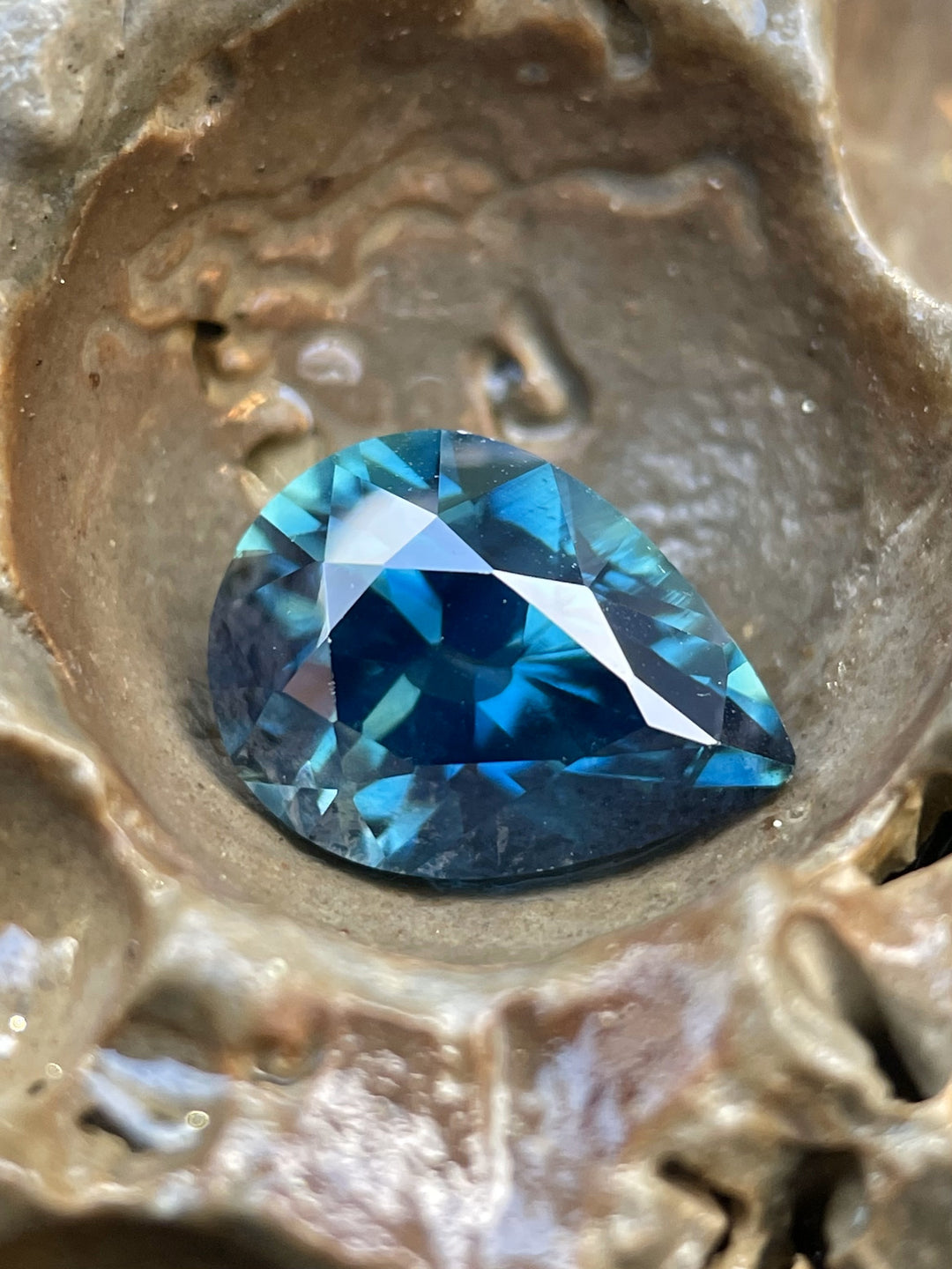 Macro photo of a 4.20ct untreated Nigerian sapphire in a pear cut, resting in a natural crevice, highlighting its rich teal, blue, and green saturation.