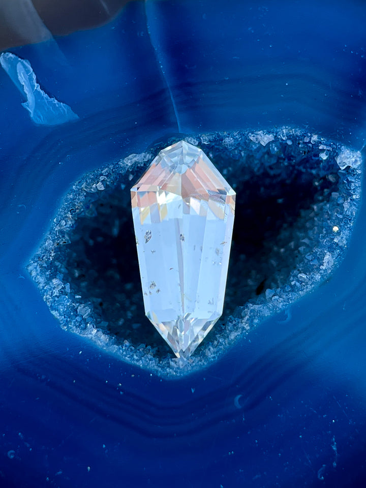 A mesmerizing 1.90-carat pale seafoam sapphire resting on a deep blue crystal surface, emphasizing its custom step cut shield design and stunning clarity.
