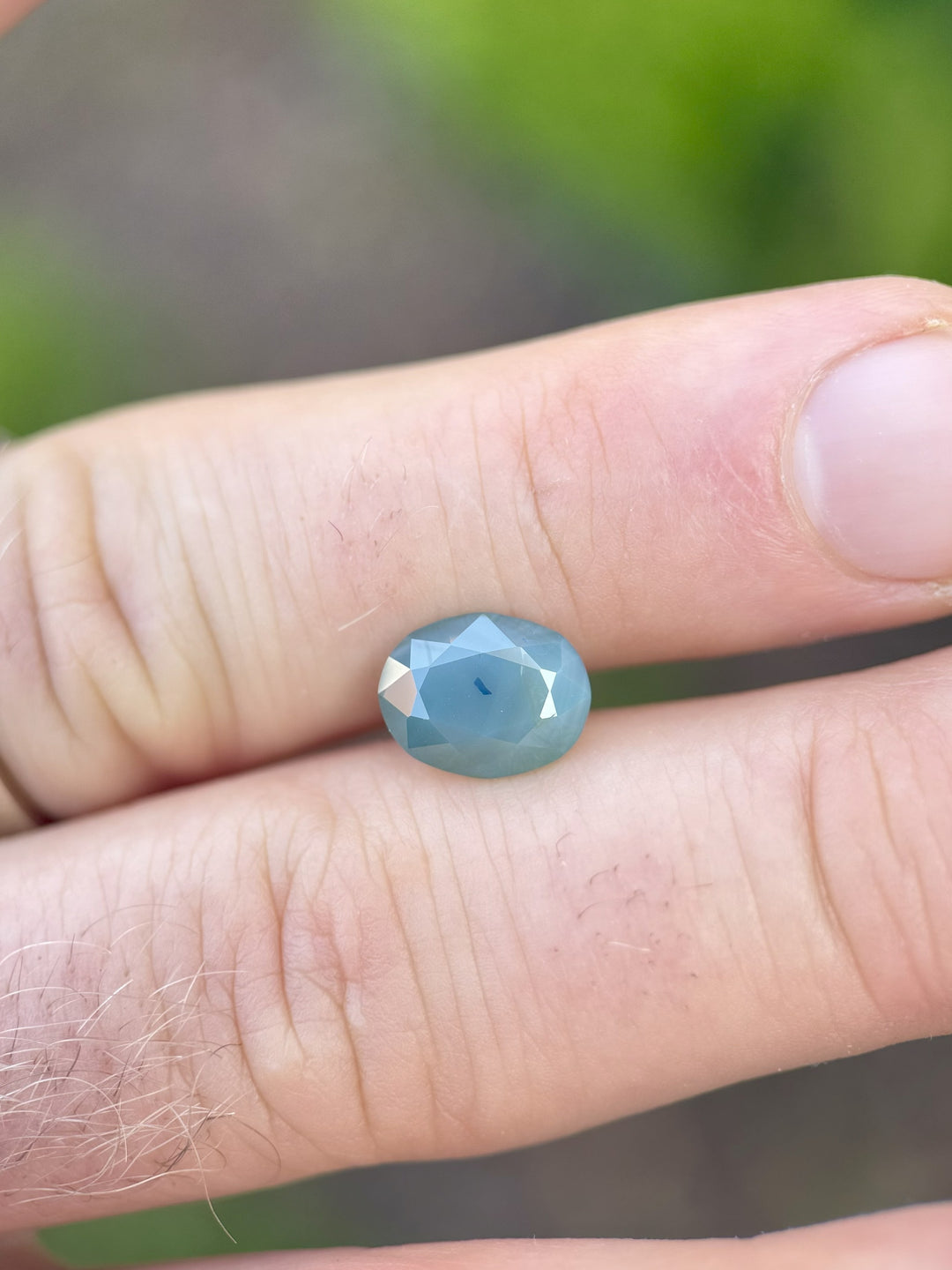 Close-up of a 4.19-carat teal blue opalescent sapphire resting on fingertips, showcasing its oval mixed brilliant cut and natural luster.